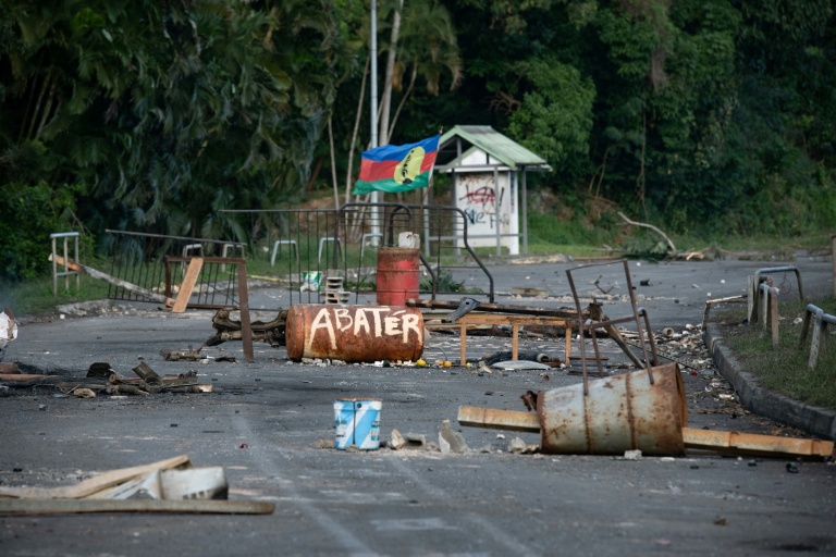Un drapeau du FLNKS parmi des débris calcinés d'un barrage routier près de Mont-Dore, en périphérie de Nouméa, le 25 juin 2024 en Nouvelle-Calédonie