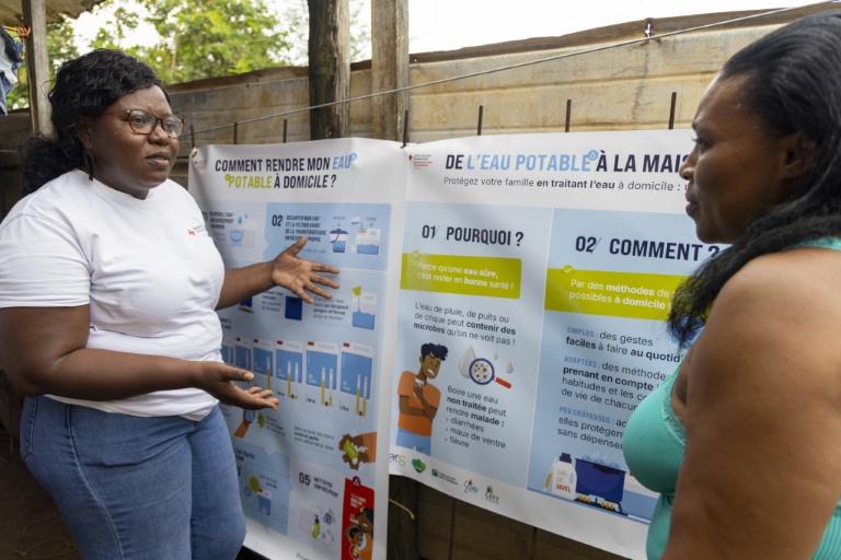 Une conseillère de la Croix-Rouge (G) explique à une habitante de Savane, un quartier de Matoury, en périphérie de Cayenne, comment traiter l'eau à domicile, le 6 juin 2026