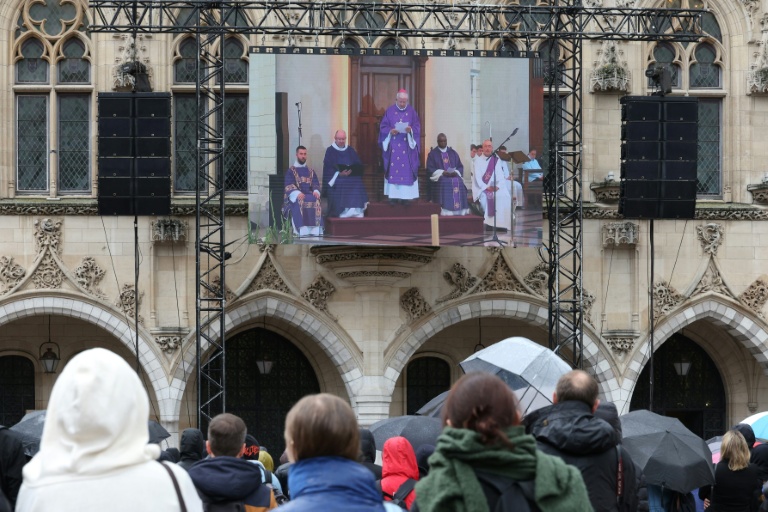 Des habitants assistent à la cérémonie d'obsèques du professeur de français Dominique Bernard, retransmise sur un écran géant installé sur la façade de l'hôtel de ville d'Arras, le 19 octobre 2023 dans le Pas-de-Calais