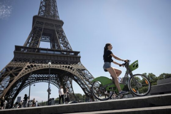 Une femme avec un vélo devant la tour Eiffel sous un soleil éclatant