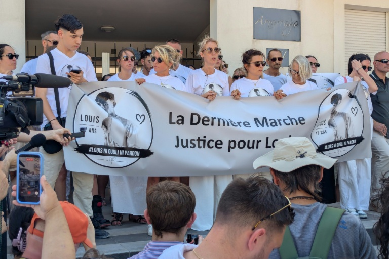 La mère de Louis (C), un adolescent de 17 ans battu à mort fin juin dans un guet-apens, se tient derrière une banderole lors d'une nouvelle marche en mémoire de son fils, le 5 juillet 2026 à Narbonne