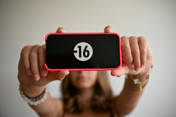 Une jeune fille montre un téléphone avec un affichage -16, symbolisant l'interdiction des réseaux sociaux aux mineurs.