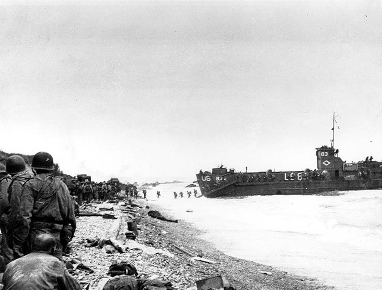 Photo de l'armée américaine, prise le 6 juin 1944, montrant des troupes du 3e bataillon du 16e régiment d'infanterie;rassemblées sur une étroite bande de la plage d'Omaha avant de progresser vers l'intérieur des terres, près de Colleville-sur-Mer, le jour J, et à l'arrière-plant le USS LCI(L)-83 débarquant d'autres hommes