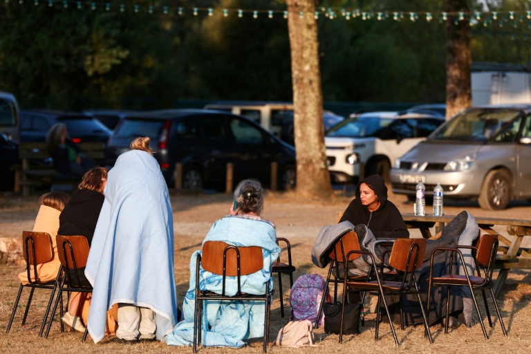 Des personnes, sac de couchage sur le dos,  sont assises devant une salle du Porge, en Gironde, après les évacuations décidées en raison de l'incendie qui sévit au nord du bassin d'Arcachon, le 23 juillet 2026