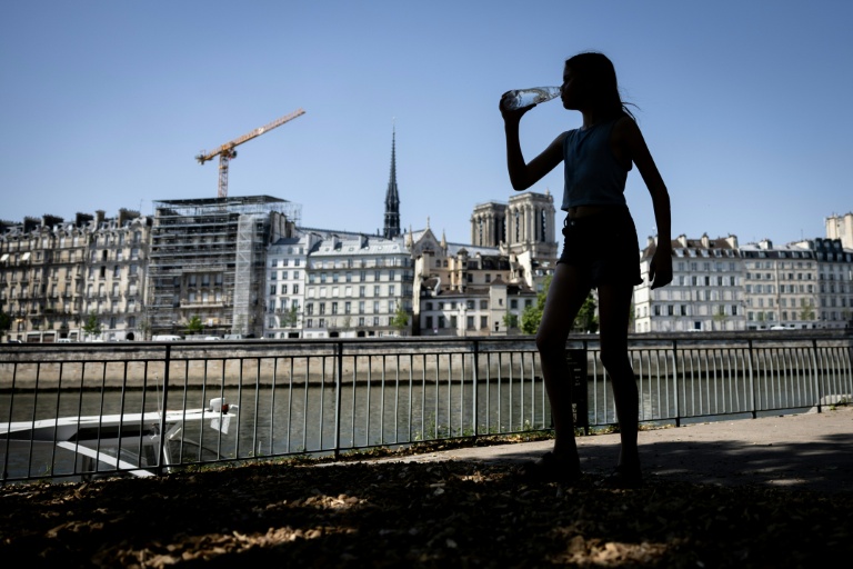 Une jeune fille boit de l'eau au bord de la Seine pendant une canicule.