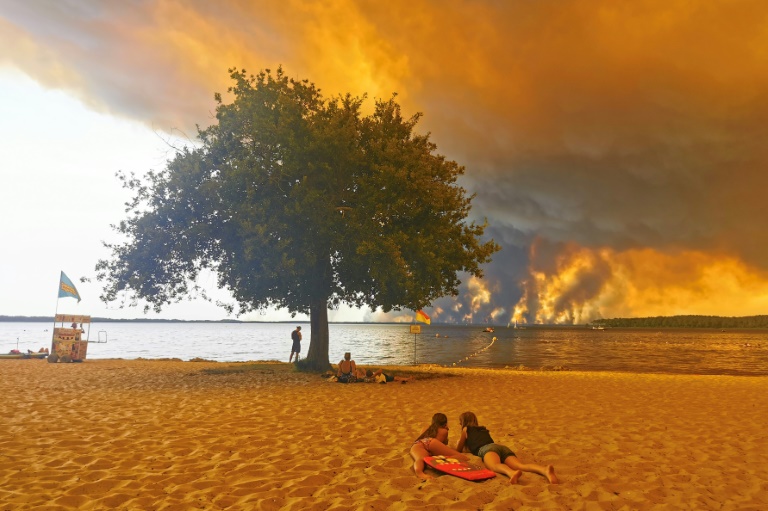 Des vacanciers sur une plage, à Lacanau, dans le sud-ouest de la France, le 24 juillet 2026, tandis que d'épais nuages de fumée s'élèvent dans le ciel au-dessus d'un incendie de forêt