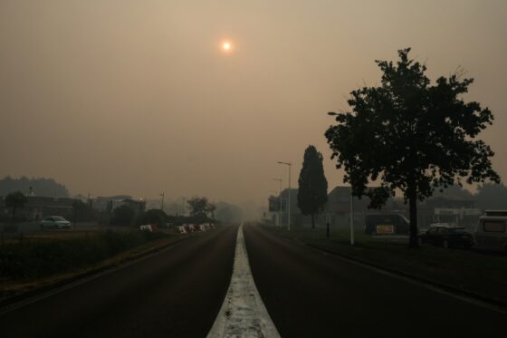 Une rue de Biscarrosse enveloppée de fumée due à un incendie, avec le soleil obscurci par la brume.