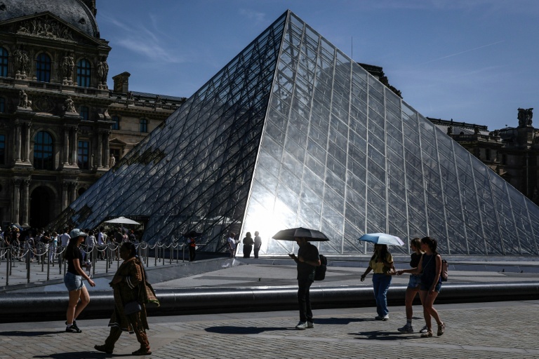 Des touristes se protègent du soleil avec des parapluies devant le musée du Louvre, le 28 mai 2026 à Paris