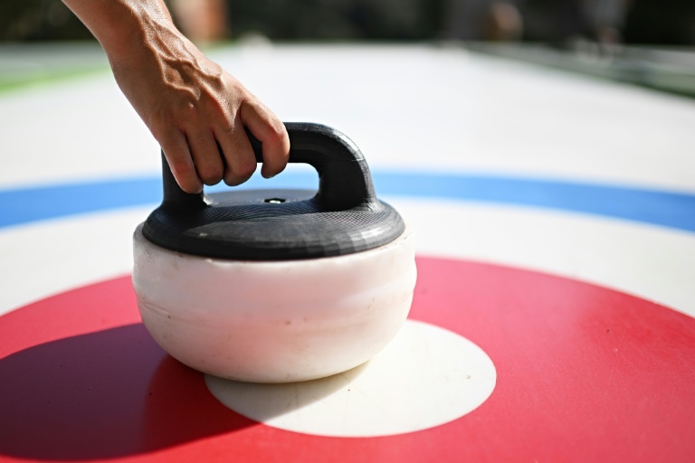 Des personnes s'essaient au curling, un sport d'hiver, sur des pistes synthétiques sans glace installées dans le parc du Colle Oppio, qui surplombe le Colisée, le 24 août 2026 à Rome