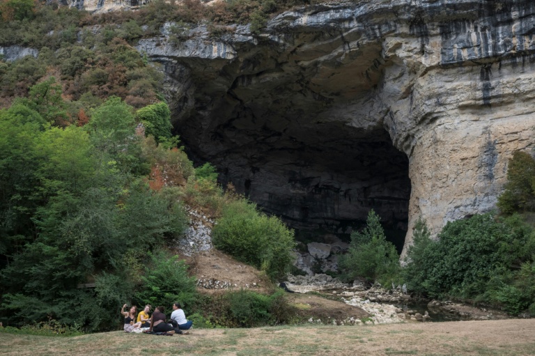 Des visiteurs sont assis près de l'une des entrées de la grotte du Mas d'Azil, en Ariège, le 5 août 2026