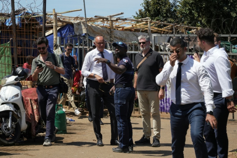 Édouard Philippe (c), fondateur et président du parti Horizons, maire du Havre et candidat à l'élection présidentielle, parle avec un policier devant un camp de réfugiés dans le village de Tsoundzou 2, à Mamoudzou, le 21 août 2026 sur l'île de Mayottte