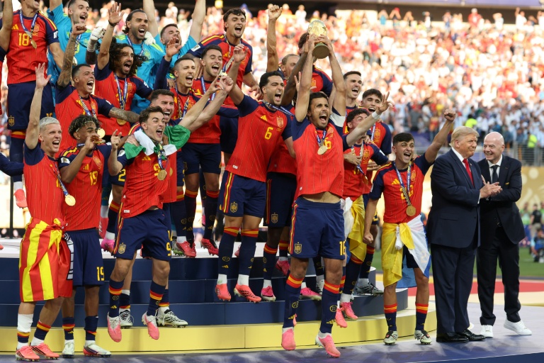 Le milieu de terrain espagnol, Rodri, brandit le trophée de la Coupe du monde aux côtés de ses coéquipiers, encadré par le président américain Donald Trump (2e à droite) et le président de la Fifa Gianni Infantino (à droite), après avoir remporté la finale du Mondial-2026 contre l'Argentine, à East Rutherford, le 19 juillet 2026