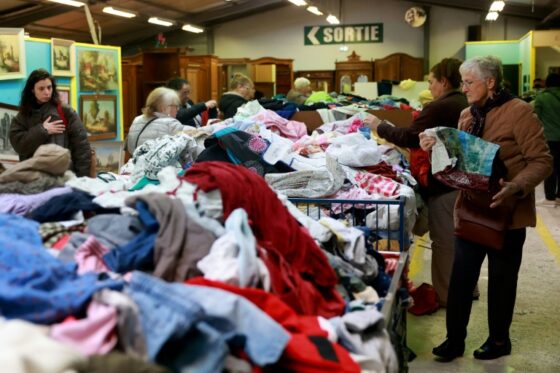 Des personnes fouillent dans des vêtements de seconde main dans une boutique.