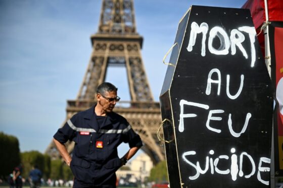 Pompiers en grève au pied de la tour Eiffel avec un cercueil affichant 'MORT AU FEU SUICIDE'.