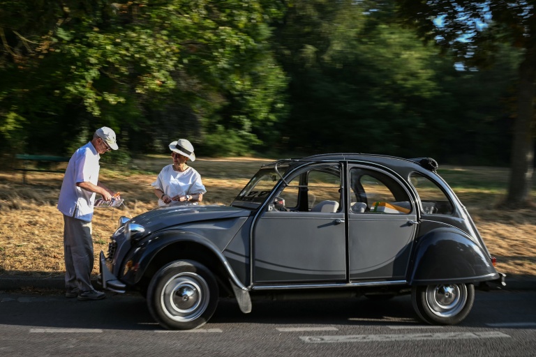 Des participants au 19ème défilé de voitures de collection de Paris à côté de leur 2CV le 19 juillet 2026 à Paris
