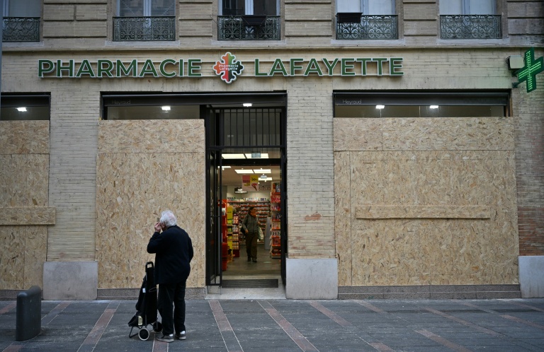 Un passant devant une pharmacie dont les vitrines ont été protégées par des panneaux de bois aggloméré, le 24 octobre 2026 à Toulouse