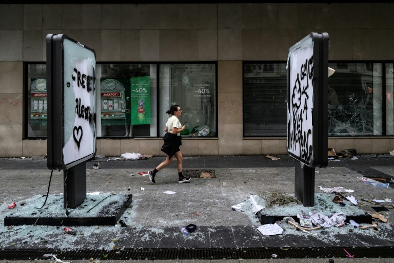 Une joggeuse passe devant des vitrines de commerces brisées et des panneaux tagués et endommages, au lendemain d'une manifestation contre la vie chère à Lyon, le 18 octobre 2026