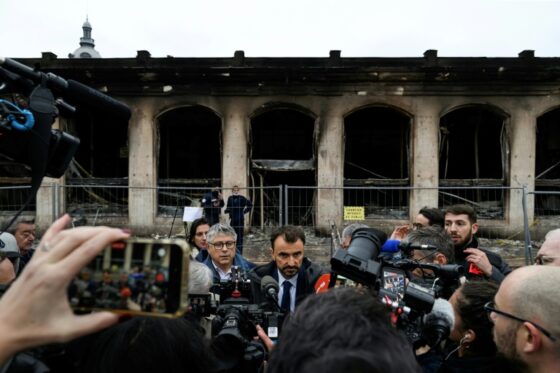 Des journalistes entourent un homme devant un bâtiment brûlé à Lyon après les manifestations du 18 octobre 2026.