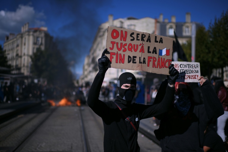 Un jeune cagoulé et vêtu de noir tient une pancarte 