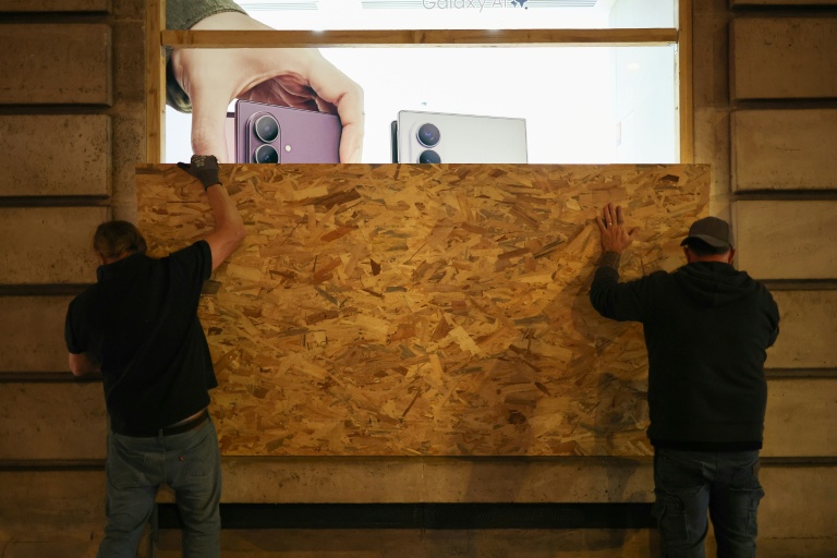 Des personnes installent un panneau en bois pour protéger une boutique de téléphonie, le 23 octobre 2026 à Paris